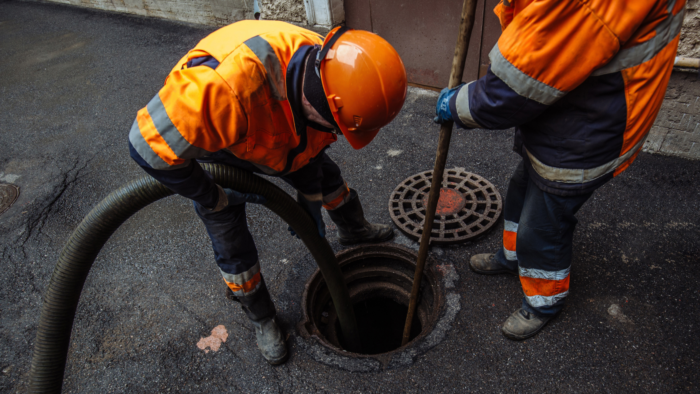 Workers cleaning a sewer in orange uniforms.