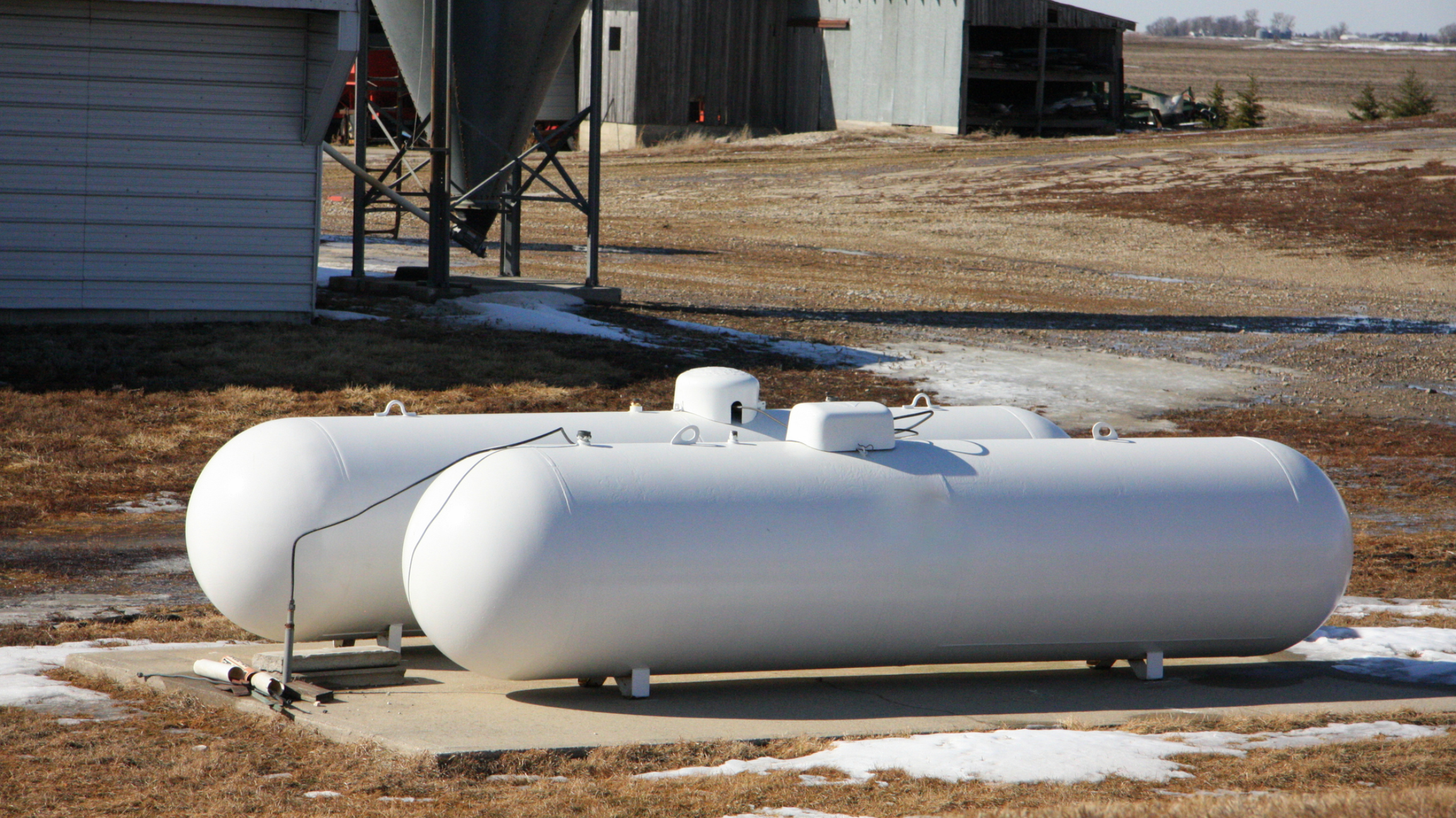 Two white propane tanks on concrete slab.