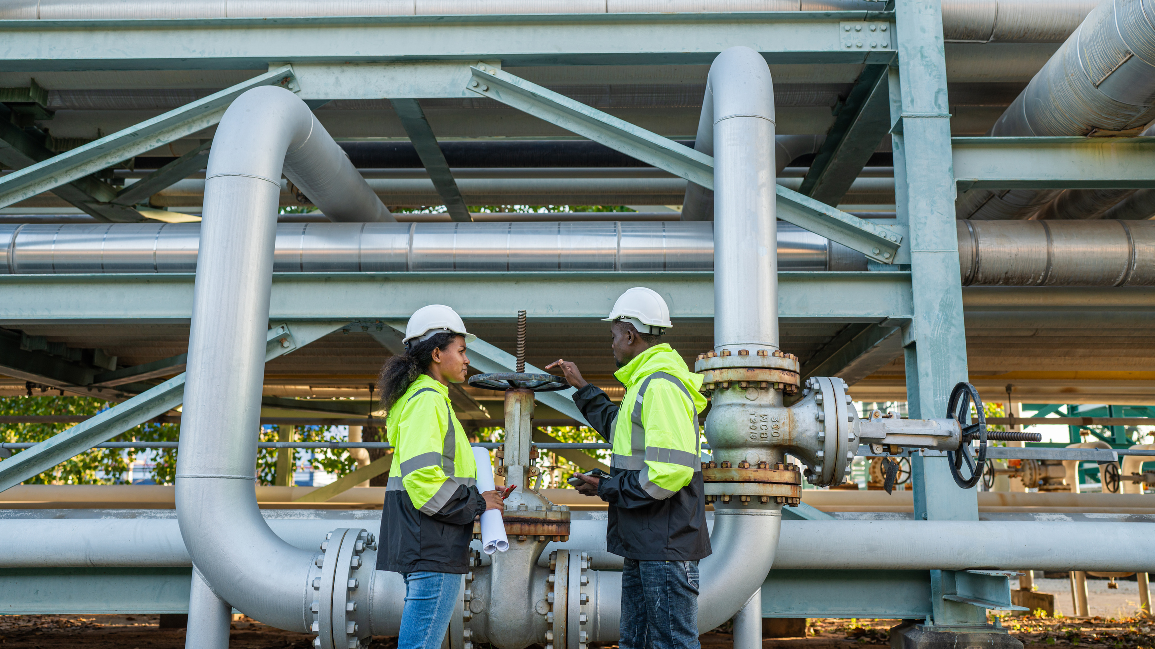 Workers inspecting industrial pipes, wearing safety gear.