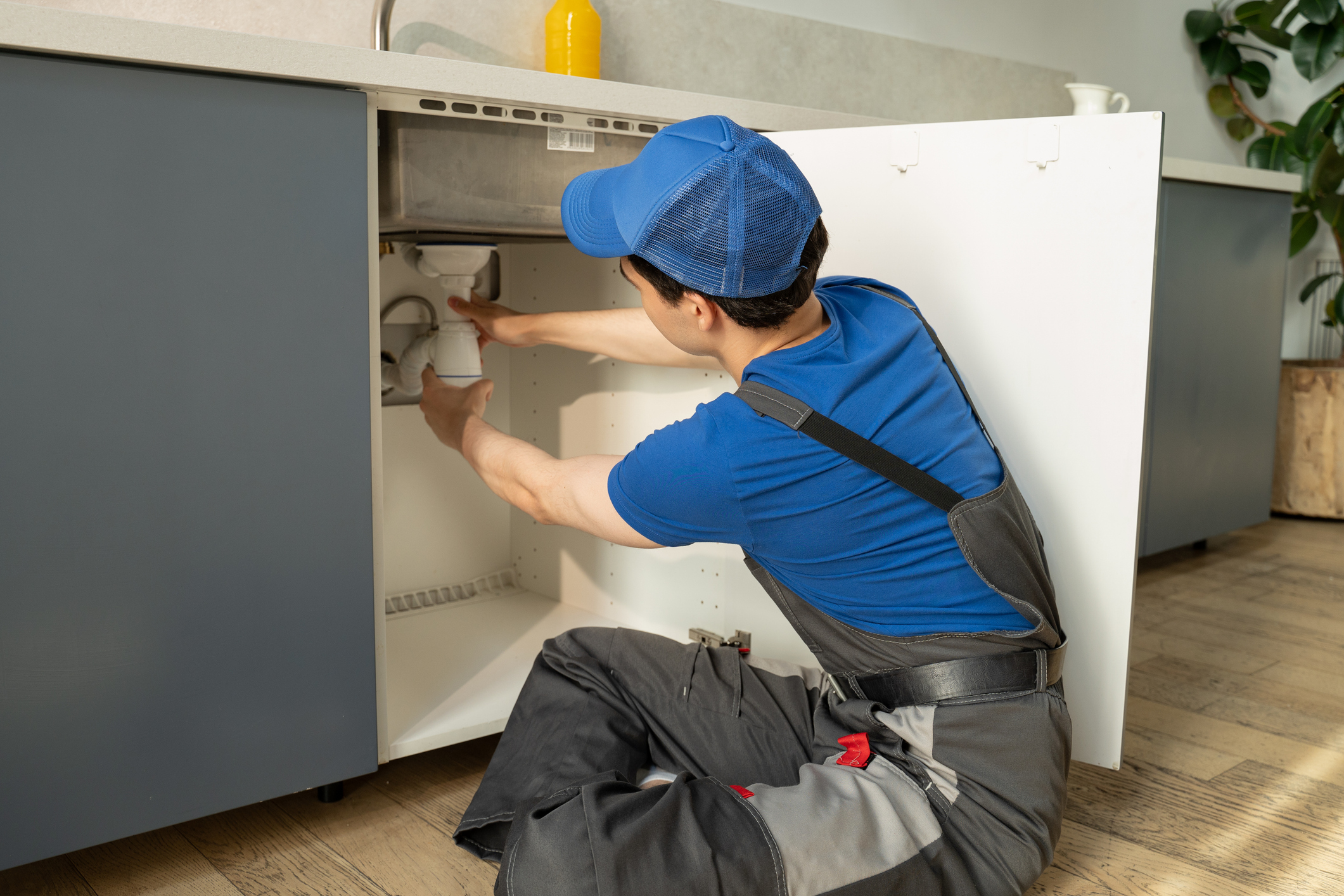 Plumber fixing sink pipes under kitchen counter.